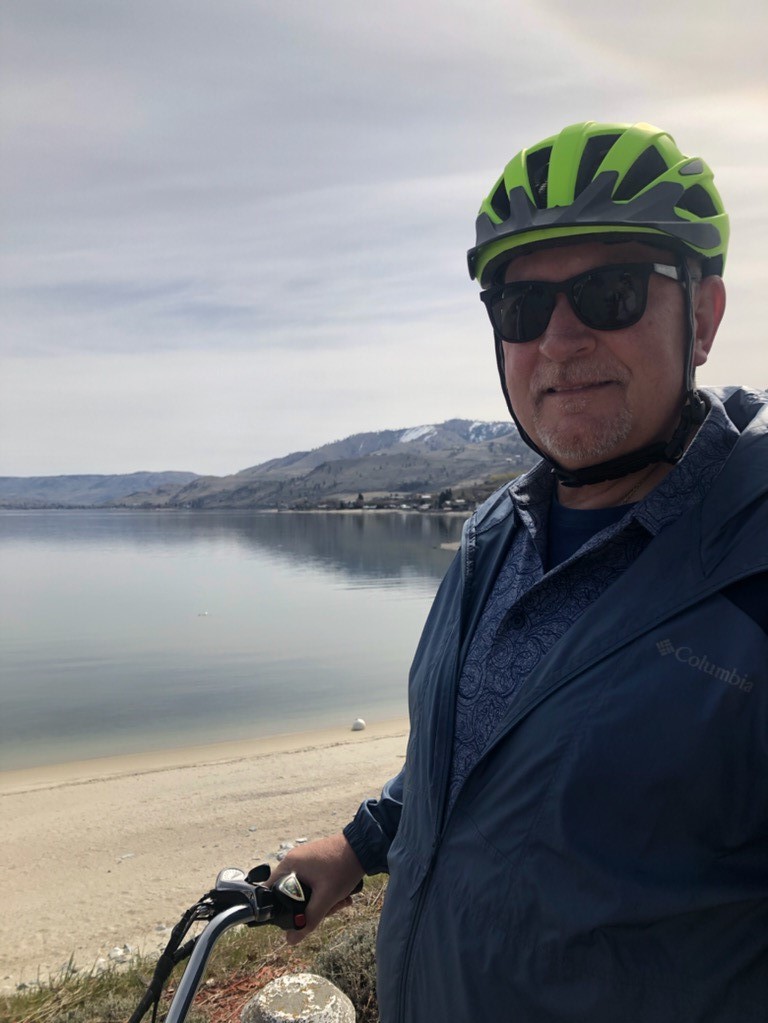 Pierce Transit CEO Mike Griffus in a bike helmet and holding the handlebar of a bike stands along a beach with foothills in the background.