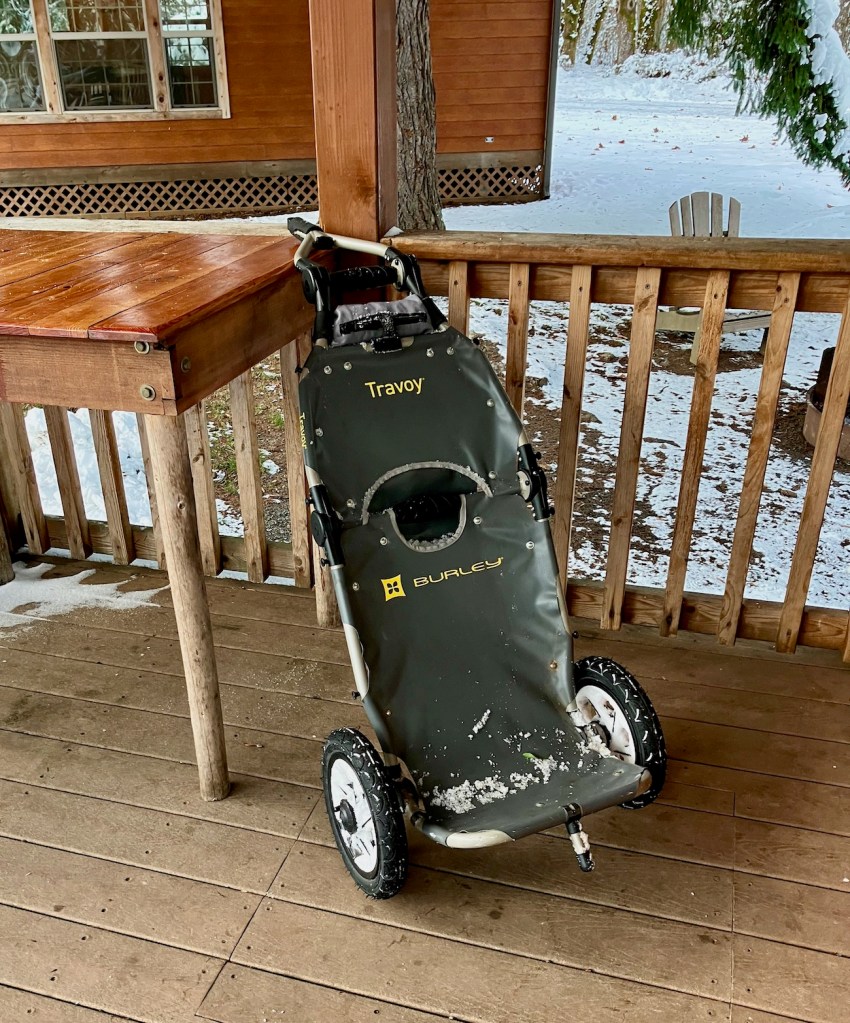 Empty Burley Travoy trailer leaning against a table on the porch of my rental cabin, with remnants of snow on it. 