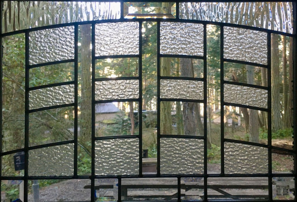 Close up of stained glass window, looking out from a camping cabin at Camano Island State Park, into the trees around the park. 
