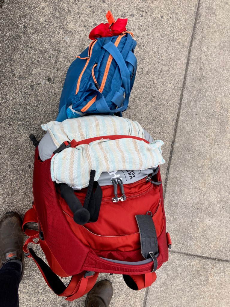 A view of my two bags sitting on the sidewalk. One is a medium sized suitcase that can be worn as a backpack and the other is a shoulder bag. 